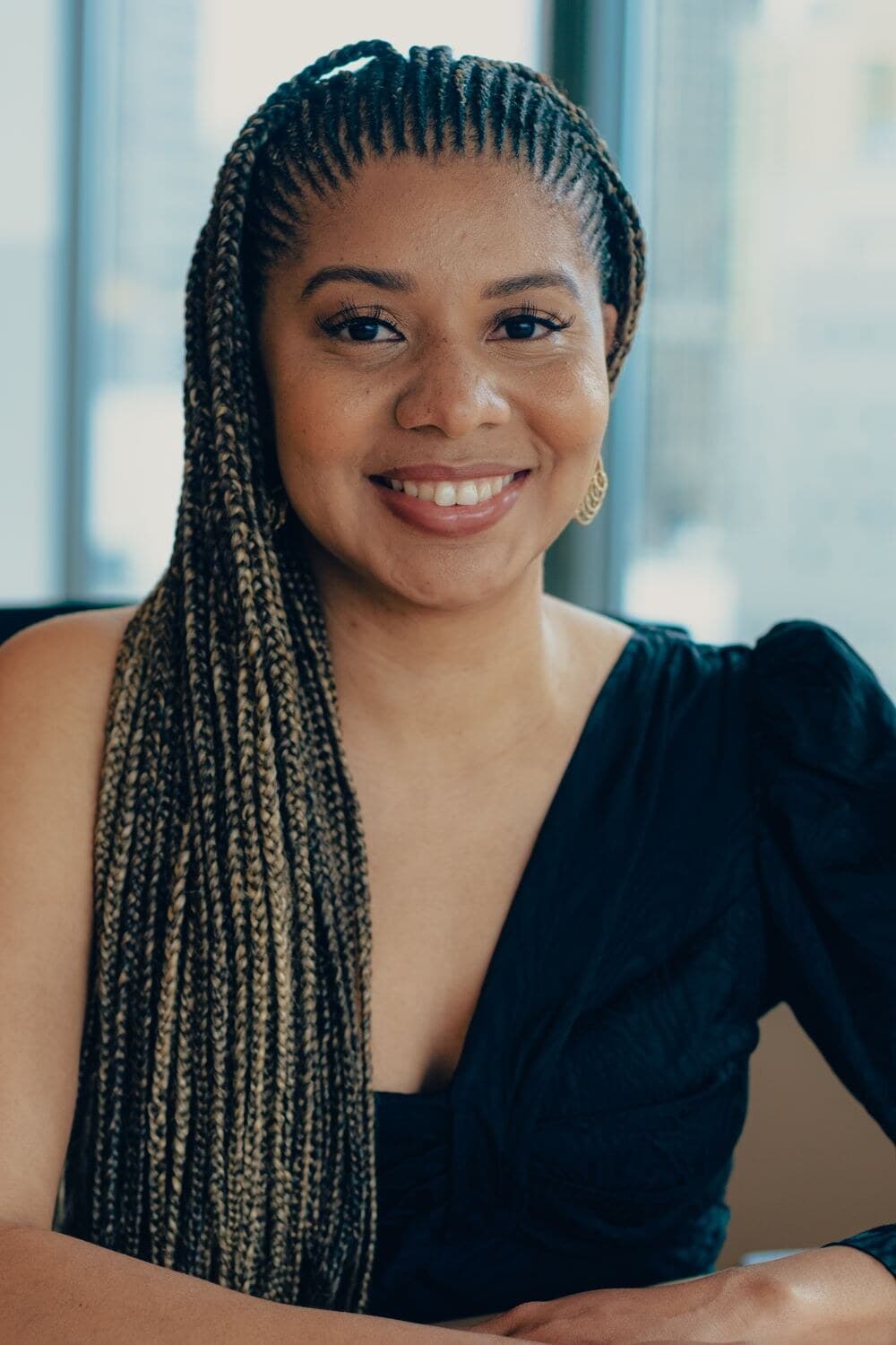 Jacqueline V. Twillie in a black dress, smiling, seated by office windows.